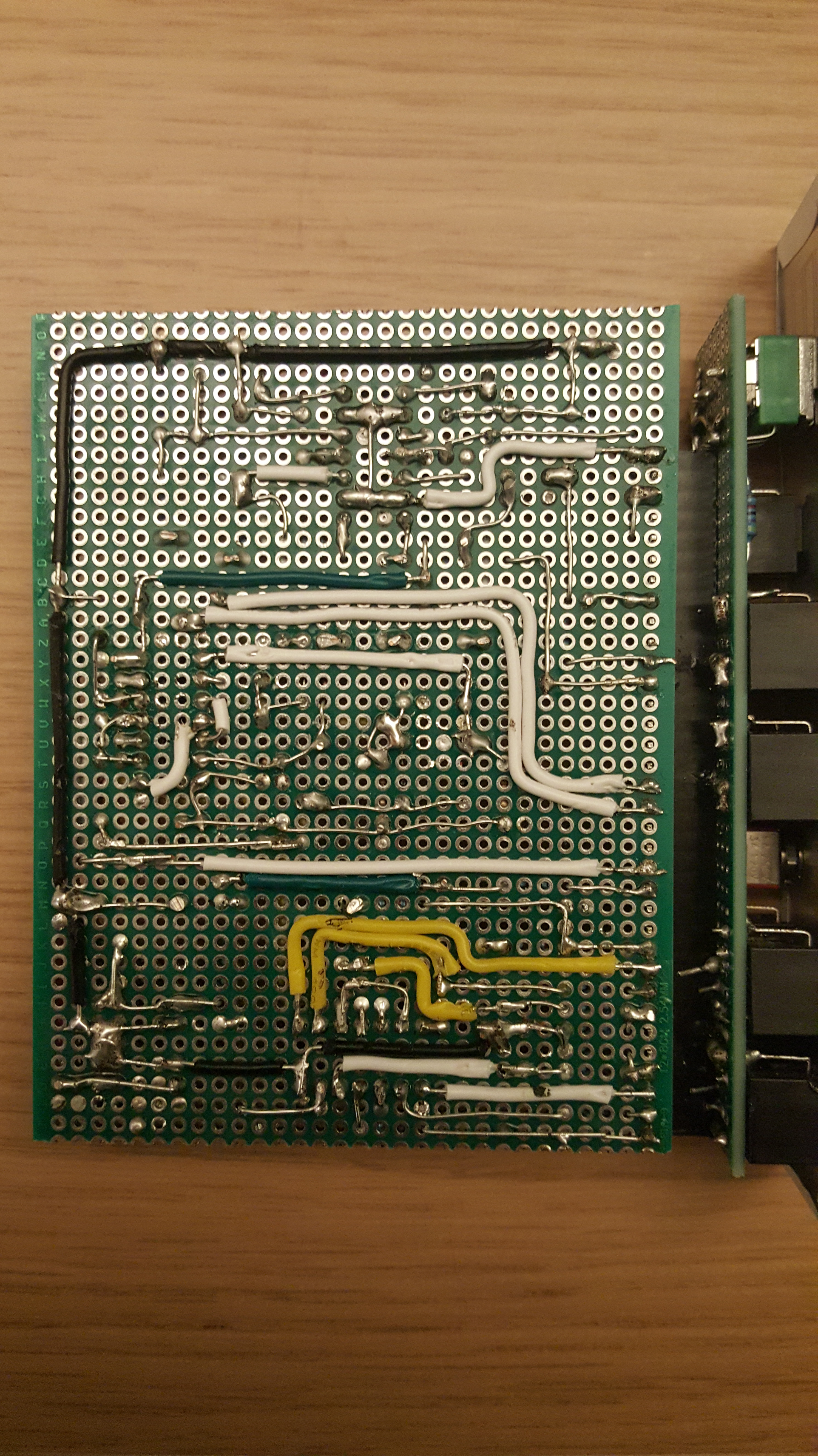 Back side of prototyping board. There are no components on this side: many component leads are bent to make connections, while other paths are made by insulated wire and solder blobs.